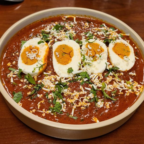 Four halved hard-boiled eggs with orange yolks in a rich red curry, garnished with cheese and cilantro.
