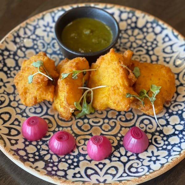 Tashan's golden fried pakoras with green chutney and pickled onions on a patterned plate.