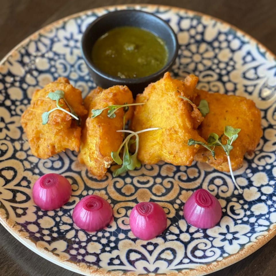 Tashan's golden fried pakoras with green chutney and pickled onions on a patterned plate.