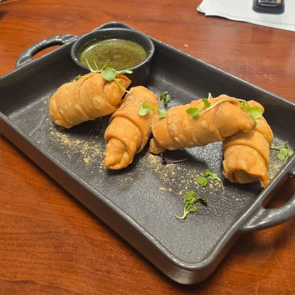 Three golden-brown, crispy Indian appetizers, possibly samosas, with green garnish and a dipping sauce.