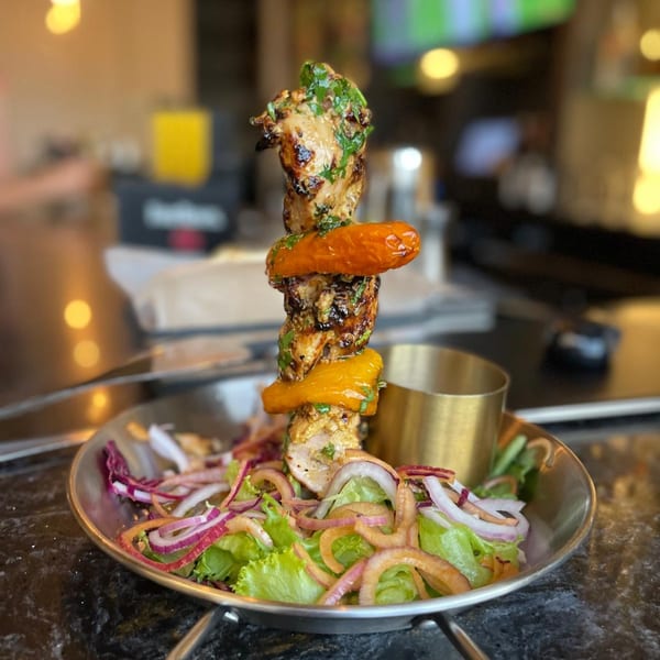 Indian chicken tikka skewer with bell peppers, cilantro, and a side salad on a metal plate.