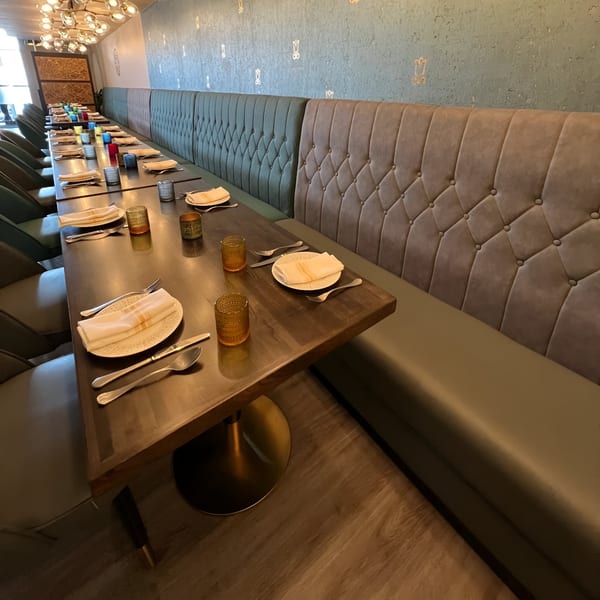 Long dining table set with plates and cutlery, flanked by tufted banquette seating at Tashan restaurant.