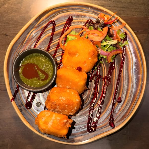Tashan's paneer pakora, a fried Indian cheese appetizer, with green chutney and salad on a decorative plate.