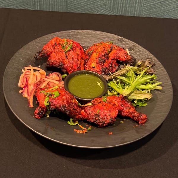 Tashan's Tandoori Chicken, vibrant red, served with green chutney, pickled onions, and fresh greens.