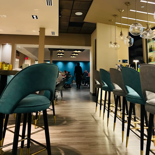 Interior of Tashan restaurant with teal bar stools, golden pendant lights, and a person walking towards dining area.